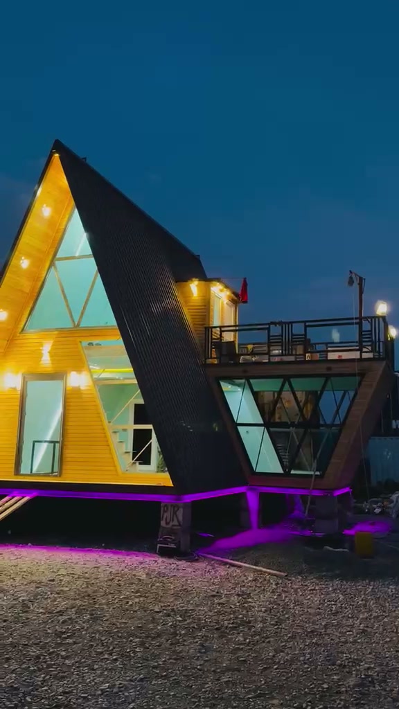 A-frame house at night with warm lighting along the roof edges and glowing triangular glazing